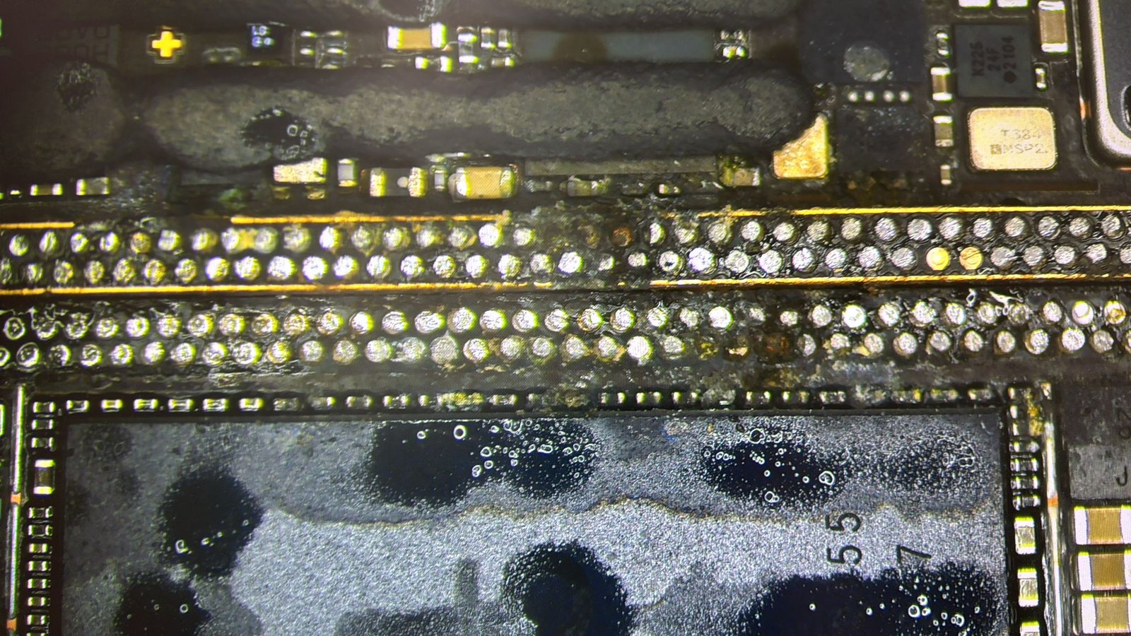 Mikroskopaufnahme: Korrosion und Rückstände an den Kontaktreihen der Hauptplatine eines iPhone 15 Pro nach Poolwasser